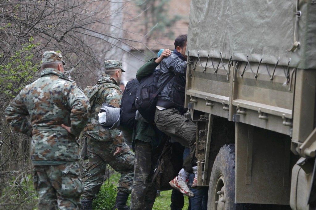 Macedonian soldiers escort migrants who have crossed the border illegally from Greece into army trucks in the village of Moini