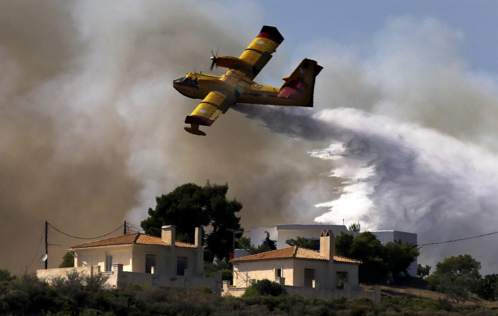 A firefighting plane drops water over a fire near holiday homes in Costa village in the Argolida region, in Southeastern Greece during a developing wild fire, July 20, 2015. Dozens of people were evacuated as firefighters fought the fire, which broke out on Monday afternoon in Panorama in Costa village at a forested area where dozens of summer houses are located, according to local media. REUTERS/Yannis Behrakis